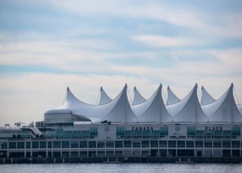 Iconic Canada Place building with its sail-like roof in Vancouver, BC against a blue sky.